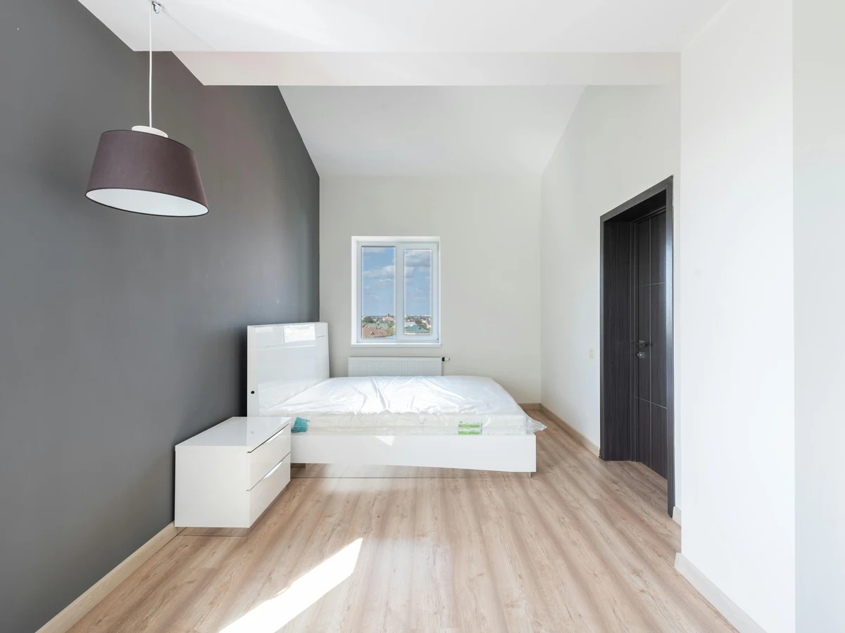 bedroom-painting-minimalist-bedroom-dark-barnstaple-decorators An empty bedroom with a dark grey wall, white walls and light wood flooring